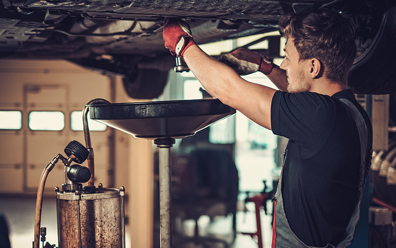 Professional technician performing under-car maintenance in a service bay.